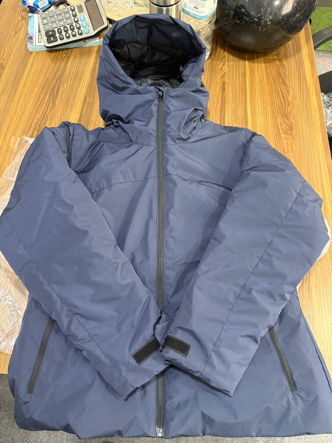 A navy hooded jacket laid closed on a wooden table with hook and loop tabs at both cuffs