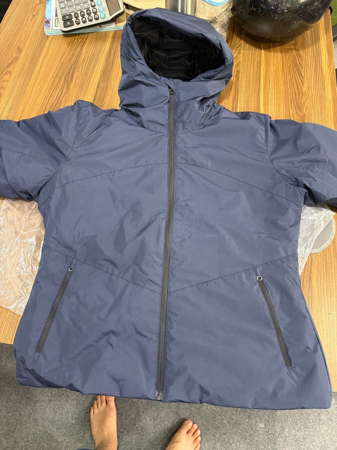 A navy hooded jacket laid flat with the hood spread open and two long zipped side pockets