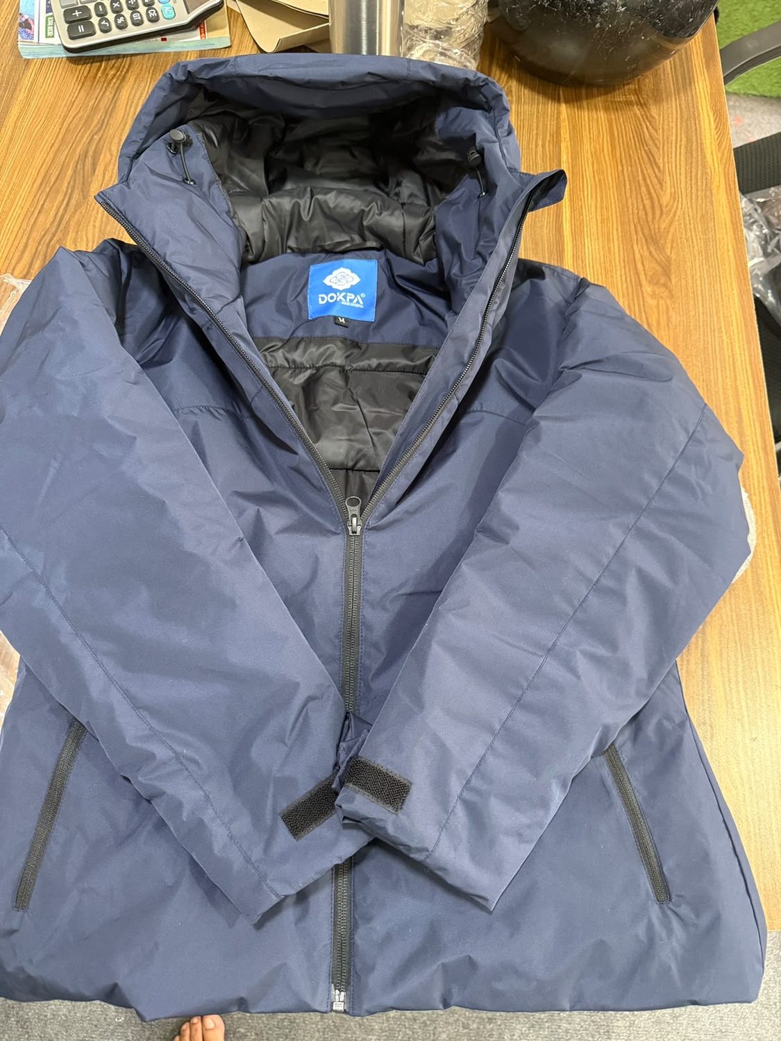 A navy jacket opened at the neck on a wooden table showing the blue Dokpa label and a small white M tag