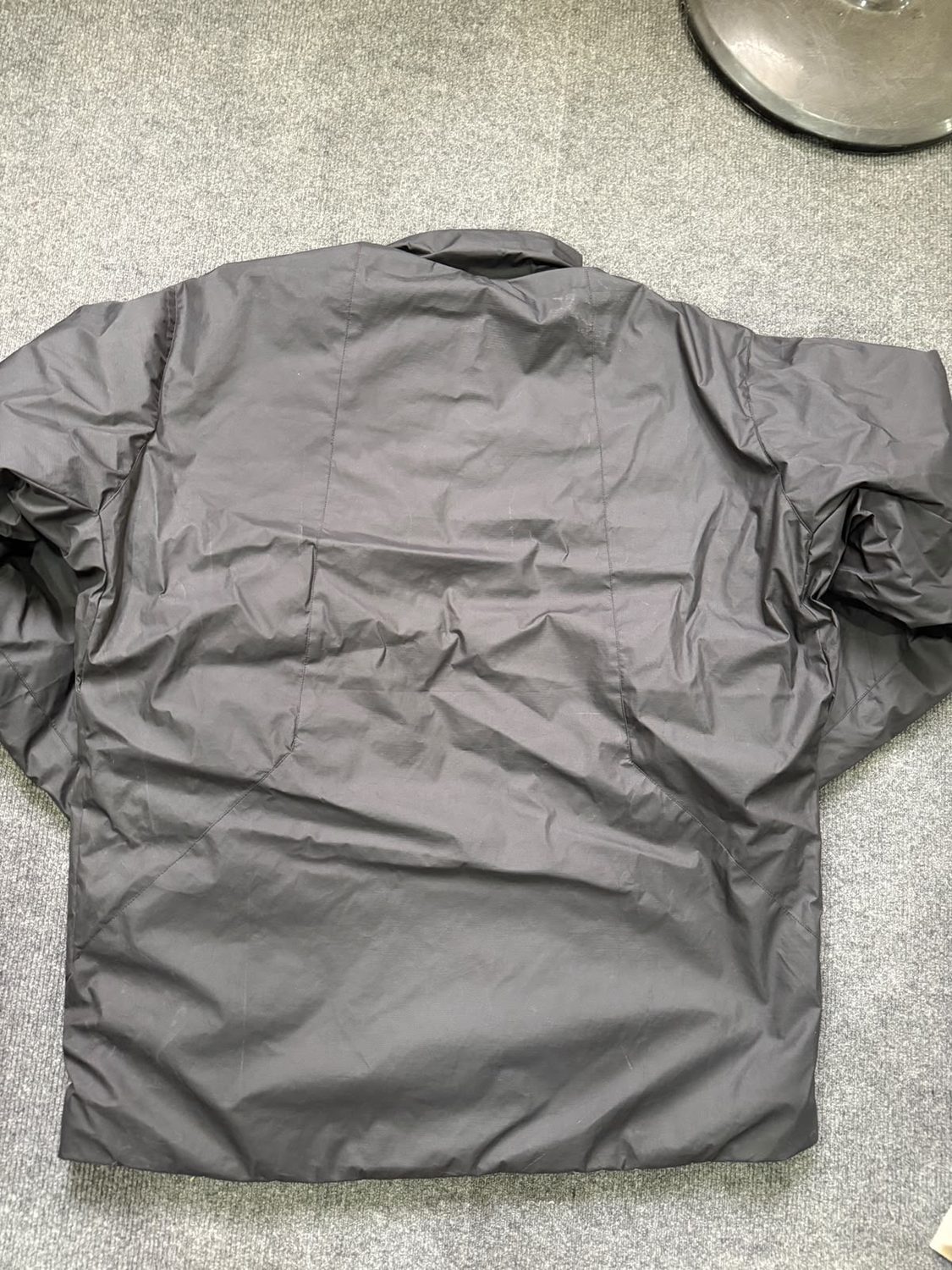 The plain back panel of a grey jacket laid flat on grey carpet