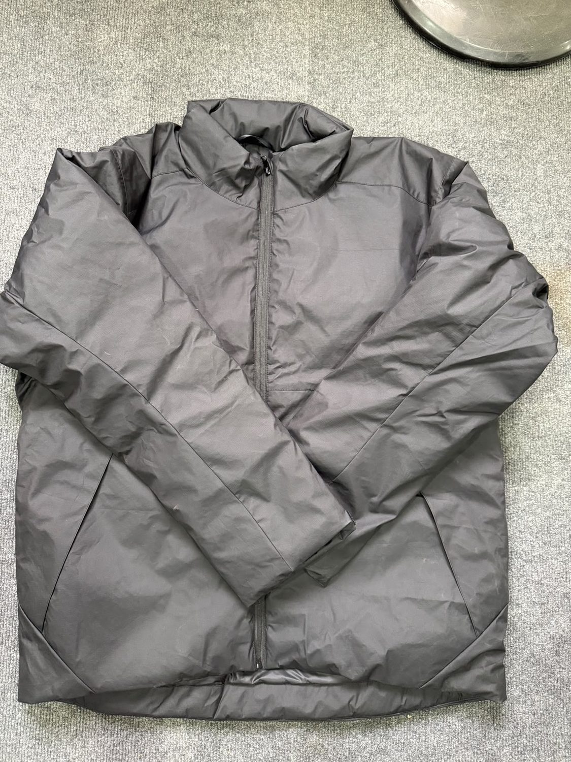 A grey jacket laid flat with a stand collar and the front zip closed