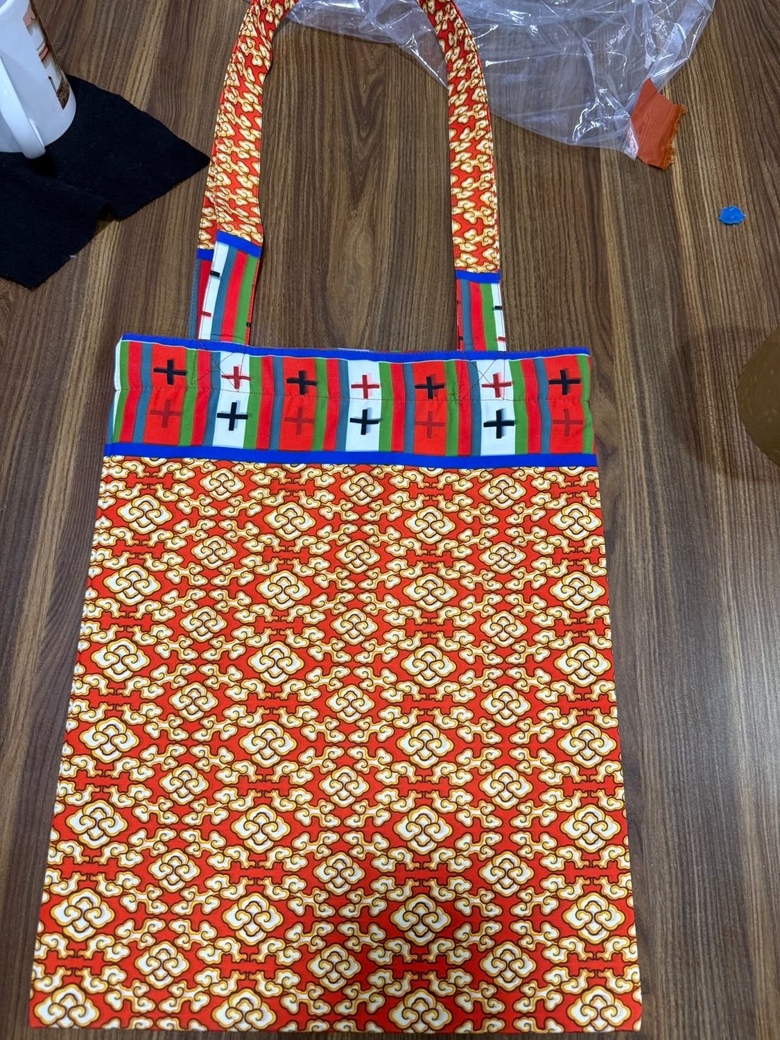 A tote bag of red and gold patterned cloth with a striped woven band across the top